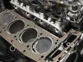 Nowa uszczelka pod głowicą czeka na montaż w silniku. Widać cylindry i fragmenty bloku silnika.