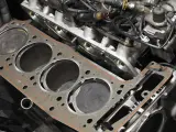 Nowa uszczelka pod głowicą czeka na montaż w silniku. Widać cylindry i fragmenty bloku silnika.