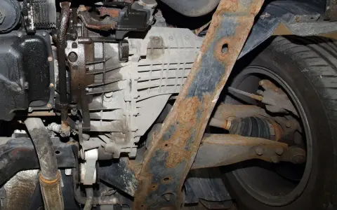 Widoczne wycieki oleju z okolic skrzyni biegów i skorodowany element zawieszenia mogą wskazywać na problemy z przegubem wewnętrznym.