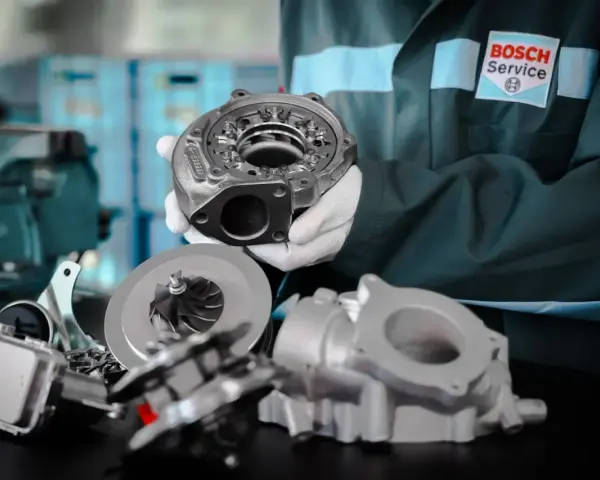 Mechanik w fartuchu Bosch Service prezentuje części turbosprężarki. Rozpoznaj uszkodzona turbina objawy i zgłoś się do serwisu.