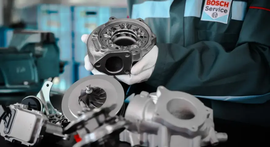 Mechanik w fartuchu Bosch Service prezentuje części turbosprężarki. Rozpoznaj uszkodzona turbina objawy i zgłoś się do serwisu.