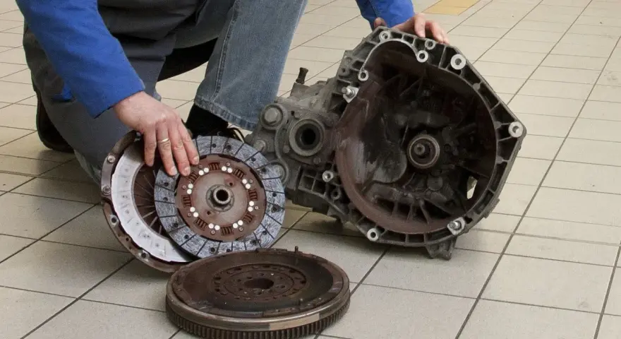 Mechanik prezentuje części po demontażu skrzyni biegów, przygotowując się do wymiany łożyska oporowego.